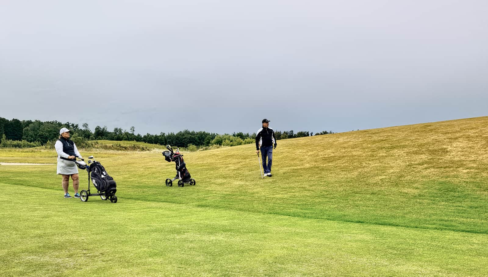 Two senior golfers walking a fairway lined with tall fescue grass in warm evening light